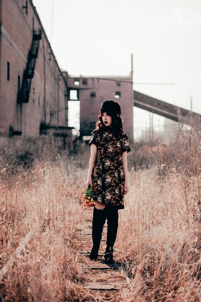 白天，穿着黑白花衣服的女人站在棕色的草地上